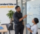 A business owner and a technical architect discussing system architecture diagrams on a glass whiteboard in an office.